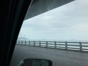 星海湾大橋を渡っているタクシーの車窓からの風景。遠くに吊橋の橋脚と水平線が見える。